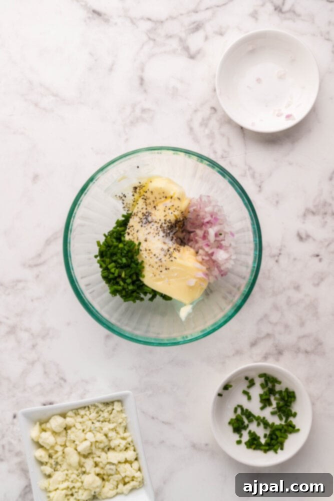 A bowl containing crumbled blue cheese, chopped herbs (chives and thyme), and softened butter, prepared for mixing.