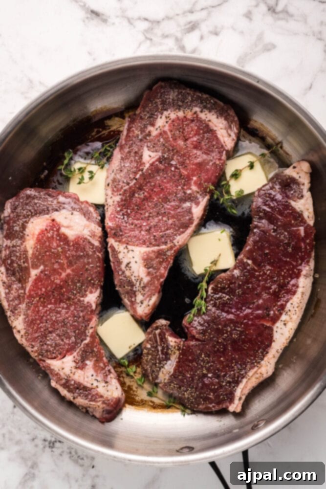 A thick New York Strip steak searing in a hot skillet with melting butter and fresh thyme.