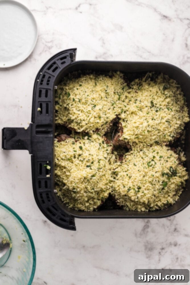 Two air-fried steaks generously topped with the Parmesan breadcrumb mixture, ready for the final cook.