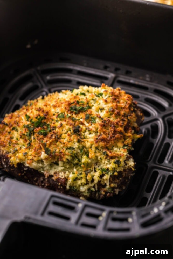 A close-up view of a golden, crispy Parmesan crusted steak cooked in an air fryer, resting on a white plate.