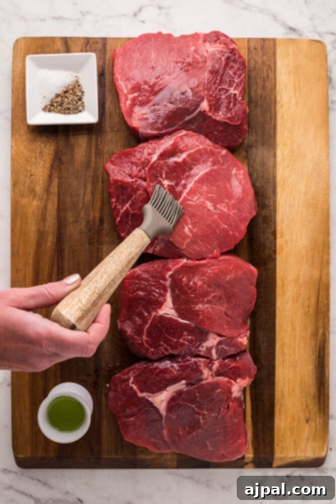 A hand expertly brushing oil onto a raw steak, preparing it for seasoning and cooking.