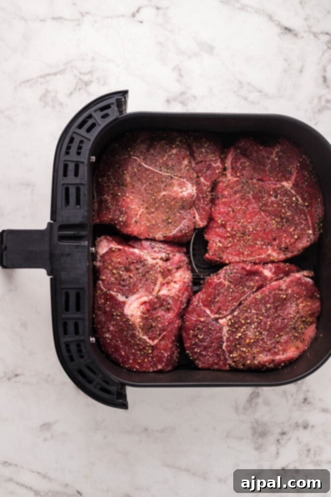 Two sirloin steaks perfectly placed inside an air fryer basket, ready for cooking.