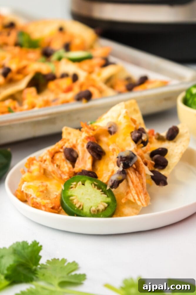 Close-up shot of Instant Pot shredded chicken nachos on a white plate, garnished with black beans and jalapeños.