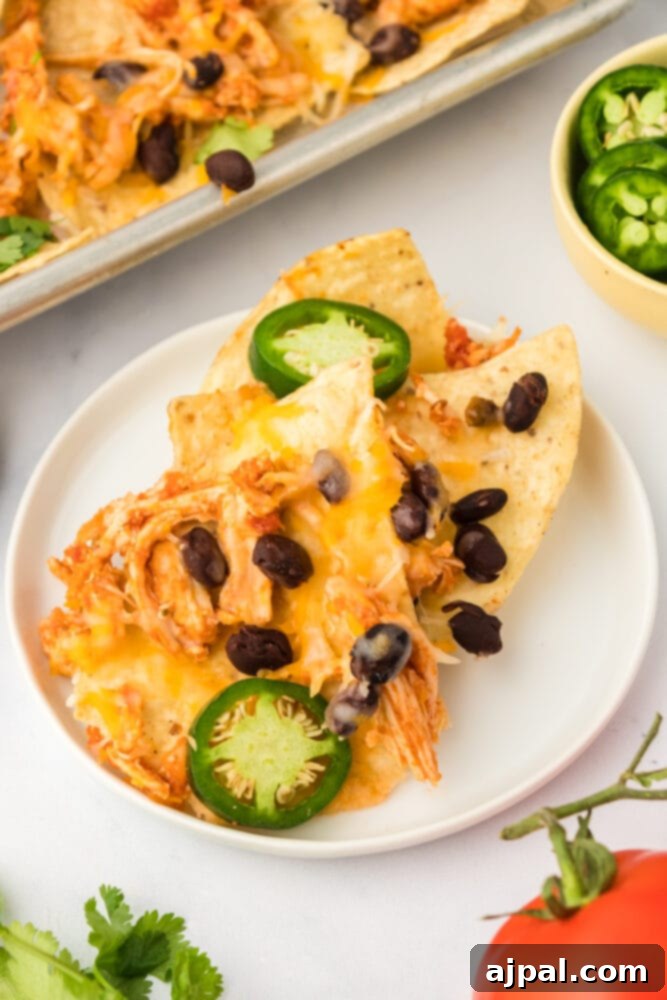 A vibrant plate of Instant Pot chicken nachos, generously topped with fresh black beans, sliced jalapeños, and a drizzle of sour cream.