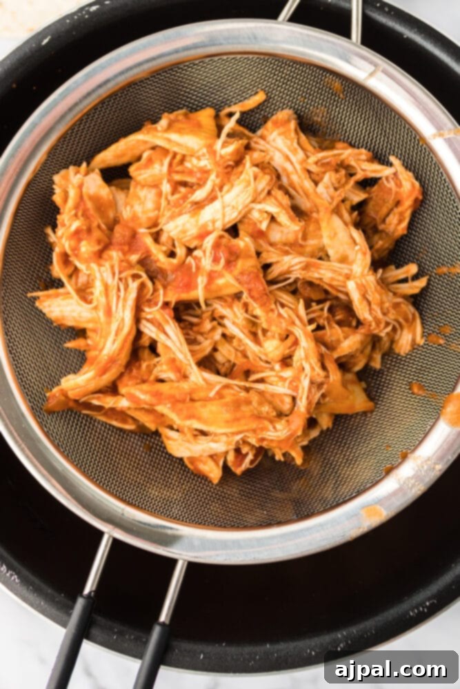 Shredded chicken being drained through a colander to remove excess liquid, preventing soggy nachos.