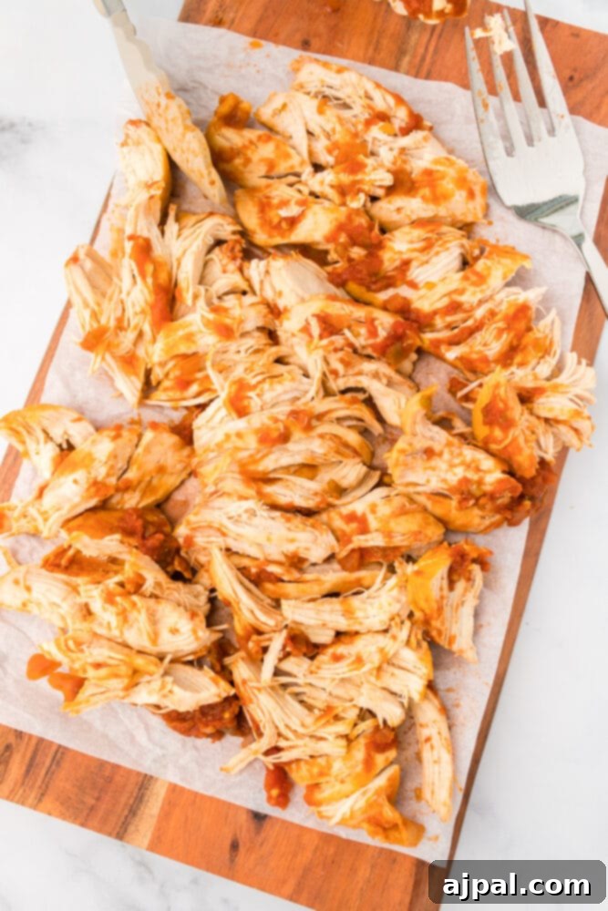 Cooked chicken breast on a cutting board, ready to be shredded with two forks.