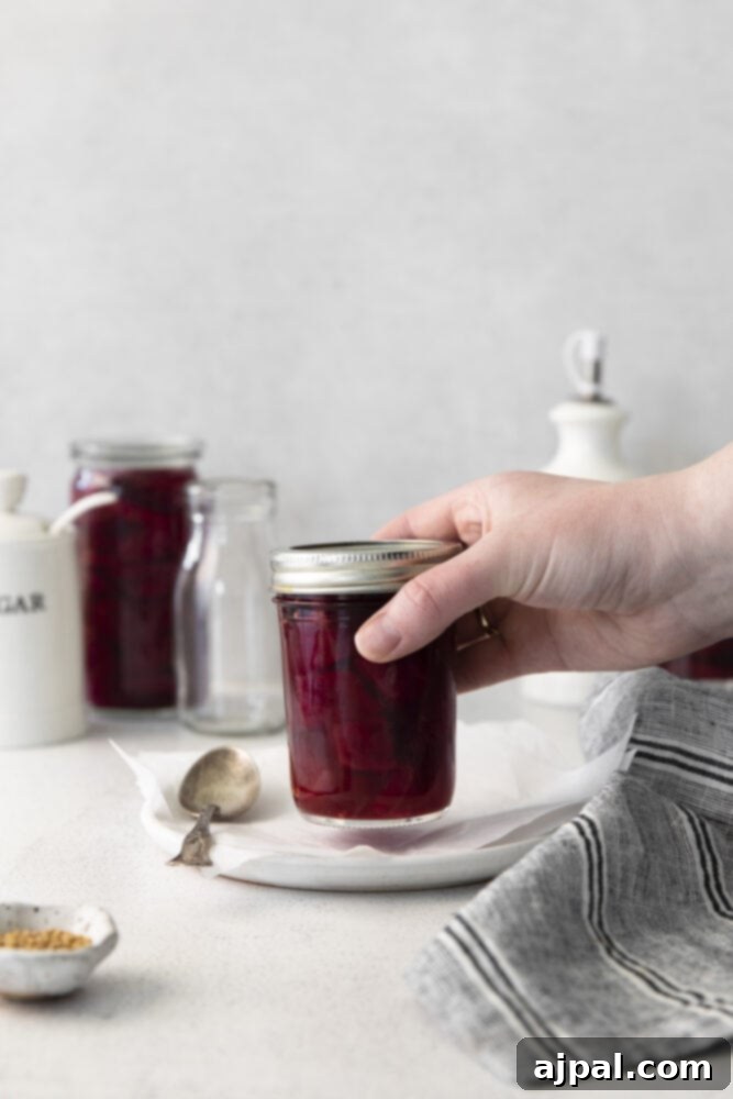 A hand reaching into a jar of pickled apple cider beets, ready to grab a tangy treat.