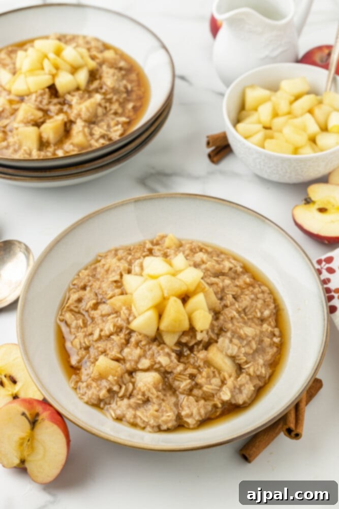 A bowl of oatmeal with apples on top and apples and more oatmeal in the background, a perfect cinnamon apple oatmeal.