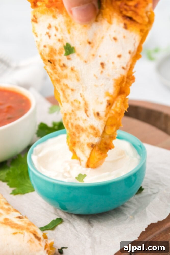 A hand dipping a chicken quesadilla wedge into a bowl of vibrant salsa