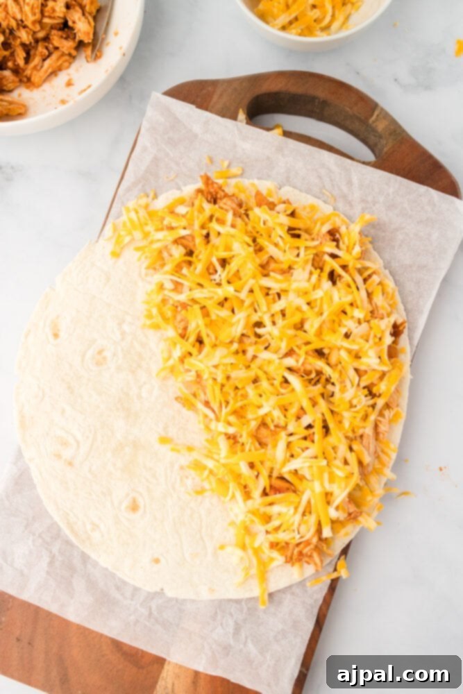 Adding shredded cheese over chicken on a tortilla before folding