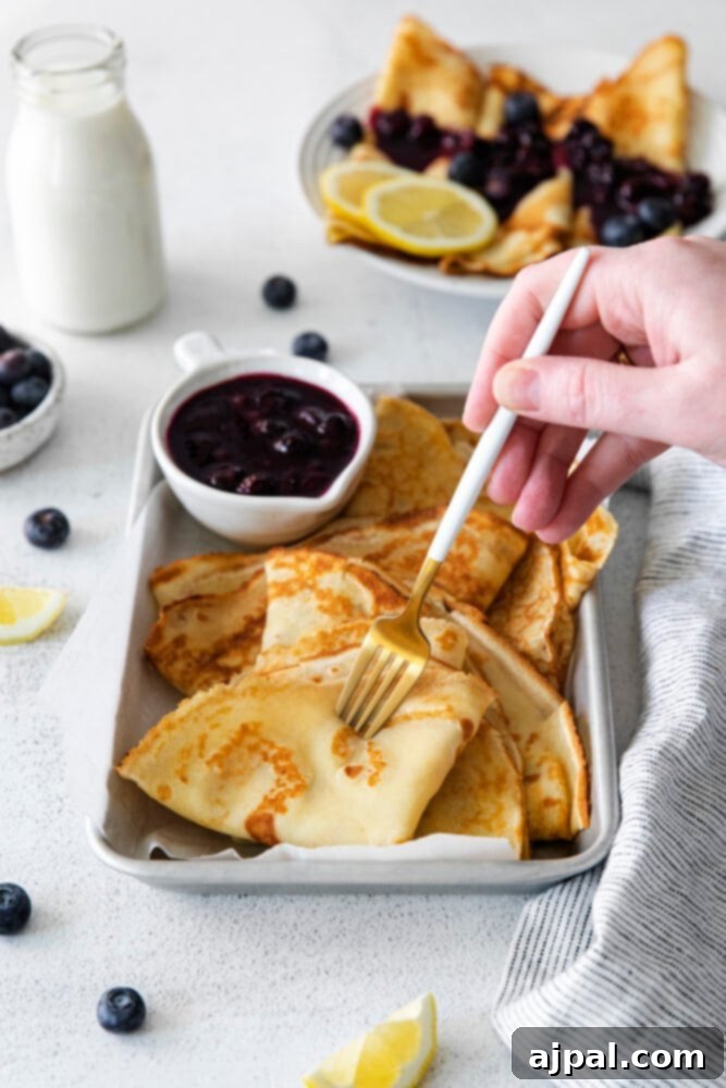Picture of exquisite Lemon Blueberry Crepes on a dish, generously drizzled with homemade blueberry sauce.