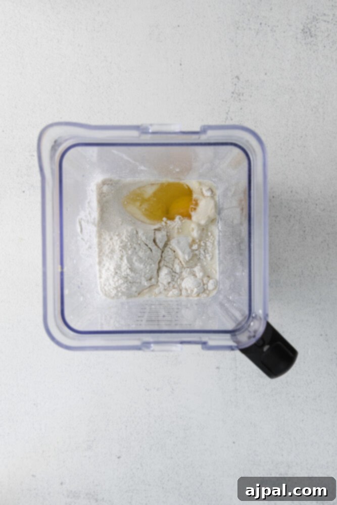A food processor beginning to mix flour and eggs for easy lemon blueberry crepes.