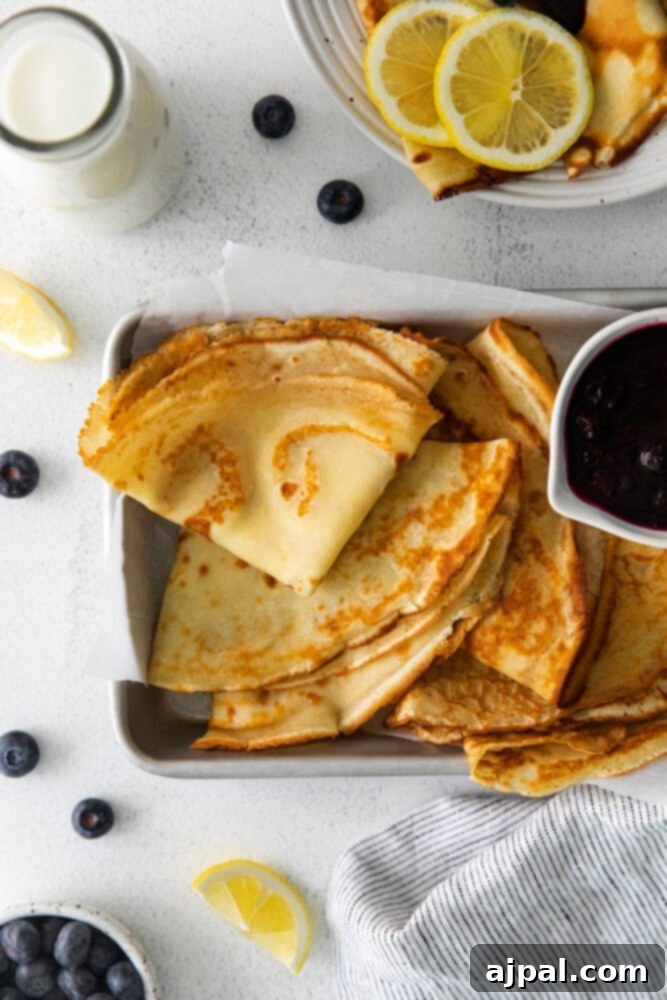 Picture of perfectly folded lemon blueberry crepes on a dish, artfully garnished with fresh blueberries and powdered sugar, ready to be served.