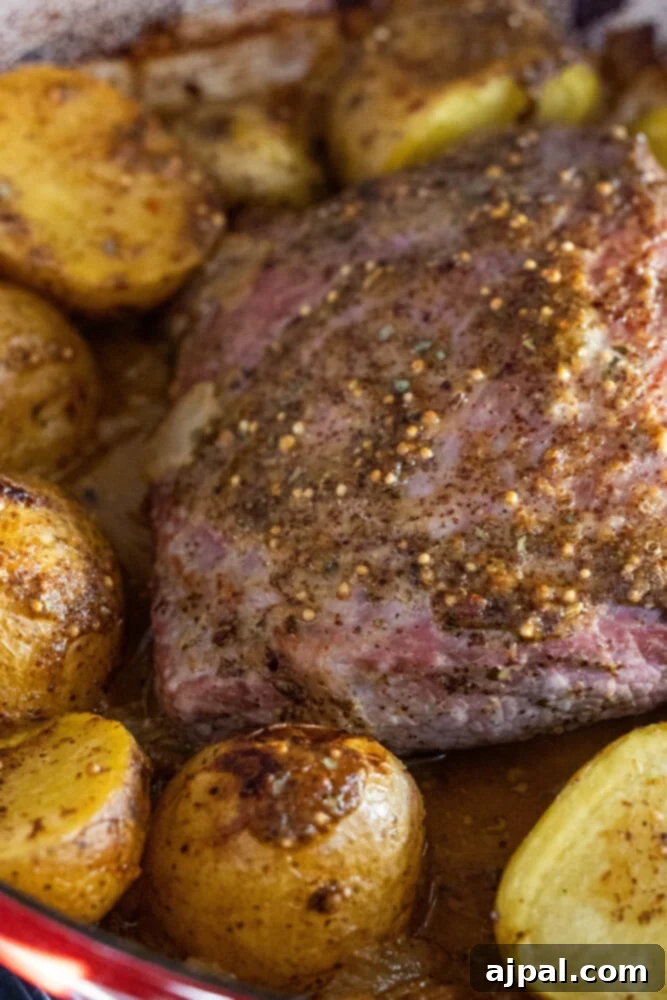 Close-up shot of the glazed corned beef and roasted potatoes on a serving platter, highlighting the rich honey mustard coating.