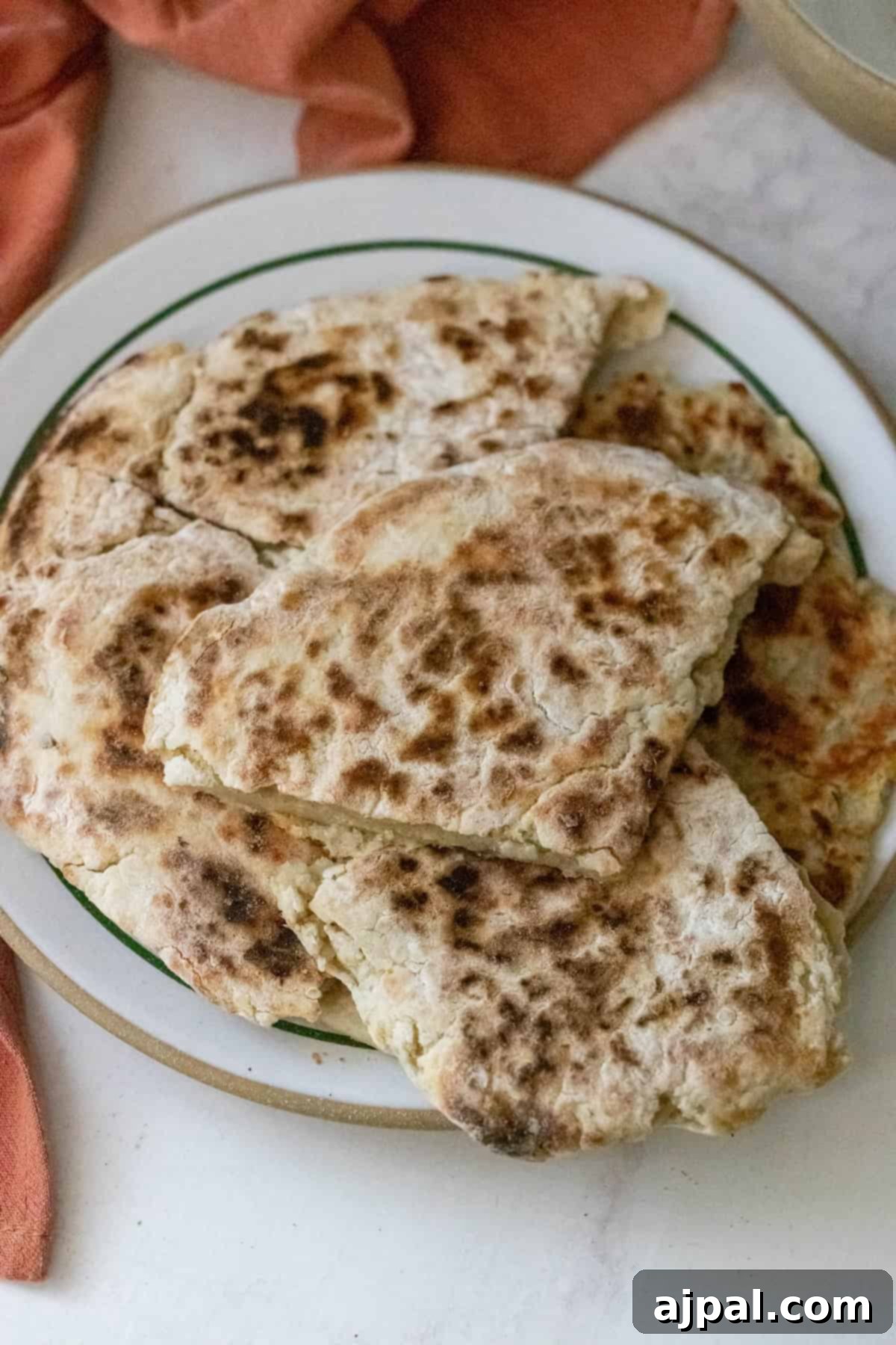 A plate of homemade skillet potato flatbreads, reminiscent of farls potato bread, is stacked on a white dish with green trim, resting on a light surface.