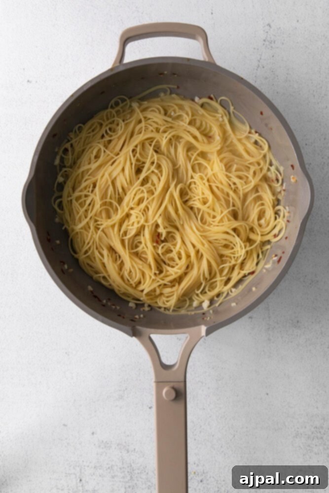 Creamy Goat Cheese and Roasted Tomato Pasta 7 Cooked angel hair pasta is being expertly tossed in a large skillet, thoroughly coated in a rich and creamy sauce, ensuring every strand is infused with flavor.