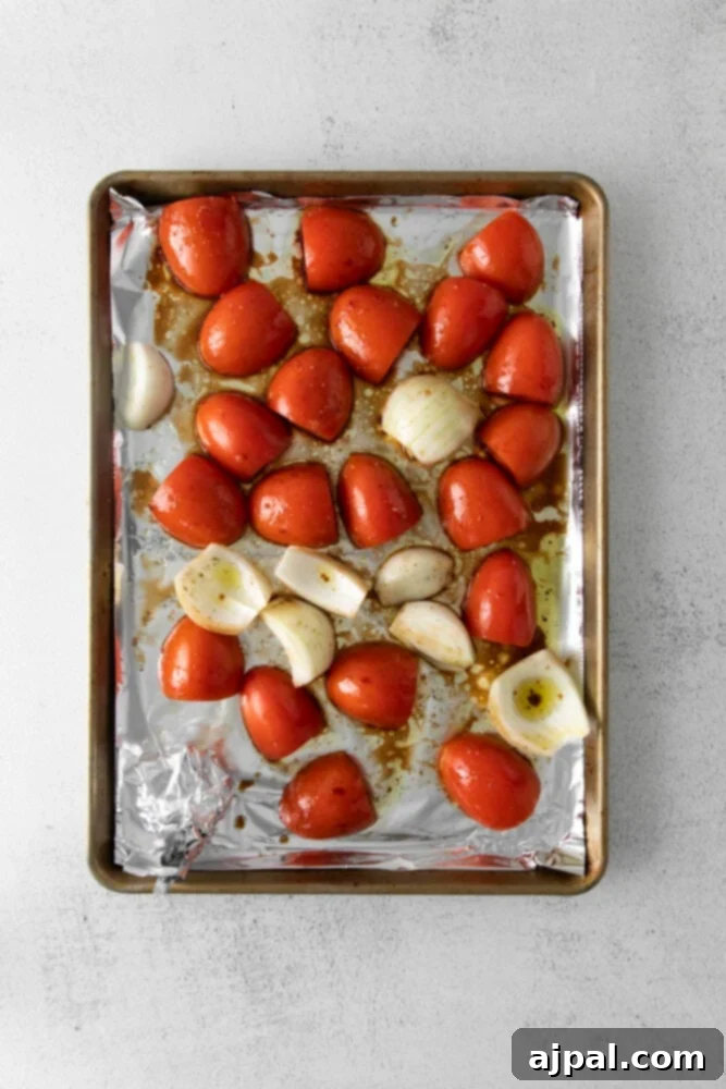 Deep Roasted Tomato Marinara 5 Fresh Roma tomatoes and quartered onions arranged on a foil-lined baking sheet before roasting.