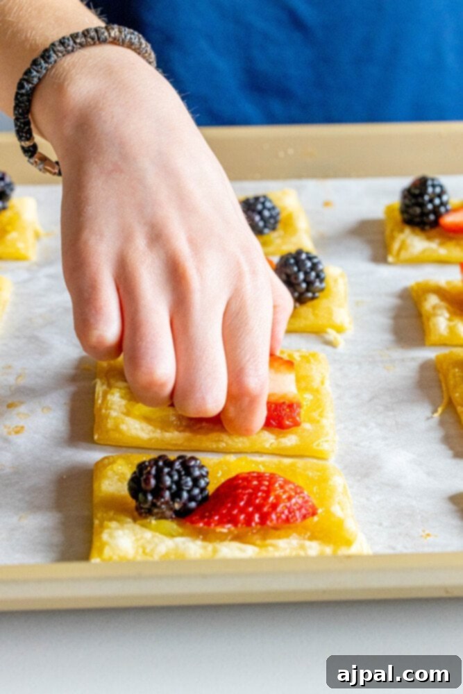 Bright Lemon Berry Tarts 7 A child's hand carefully placing a fresh strawberry and blackberry onto an unbaked lemon tart, adding a personal touch.