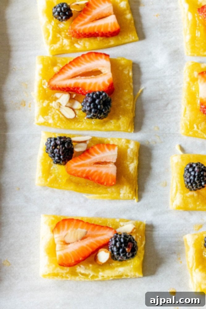 Bright Lemon Berry Tarts 9 An unbaked lemon curd tart, beautifully adorned with almonds, a strawberry, and a blackberry, presented on a baking sheet.