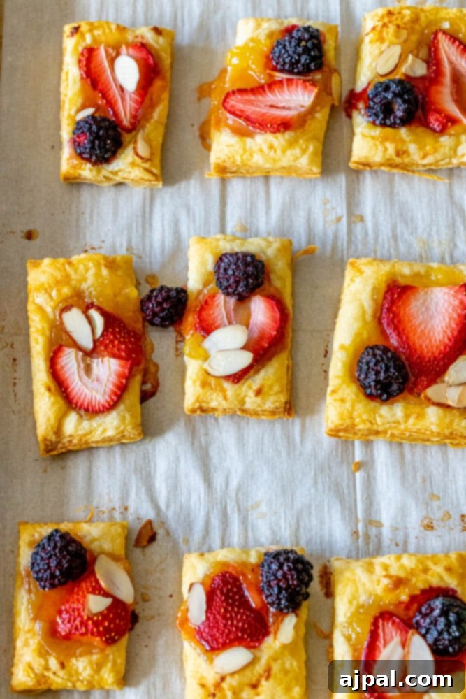 Bright Lemon Berry Tarts 10 A perfectly baked lemon curd tart, with a golden crust, topped with an almond, strawberry, and blackberry, cooling on a baking sheet.