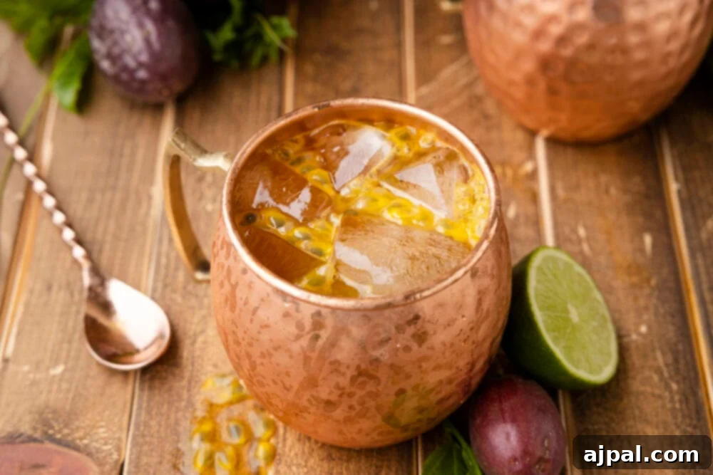 Dark Tropics Tempest 2 Passion Fruit Dark and Stormy cocktail in a copper mug, garnished with lime and mint, on a wooden surface.