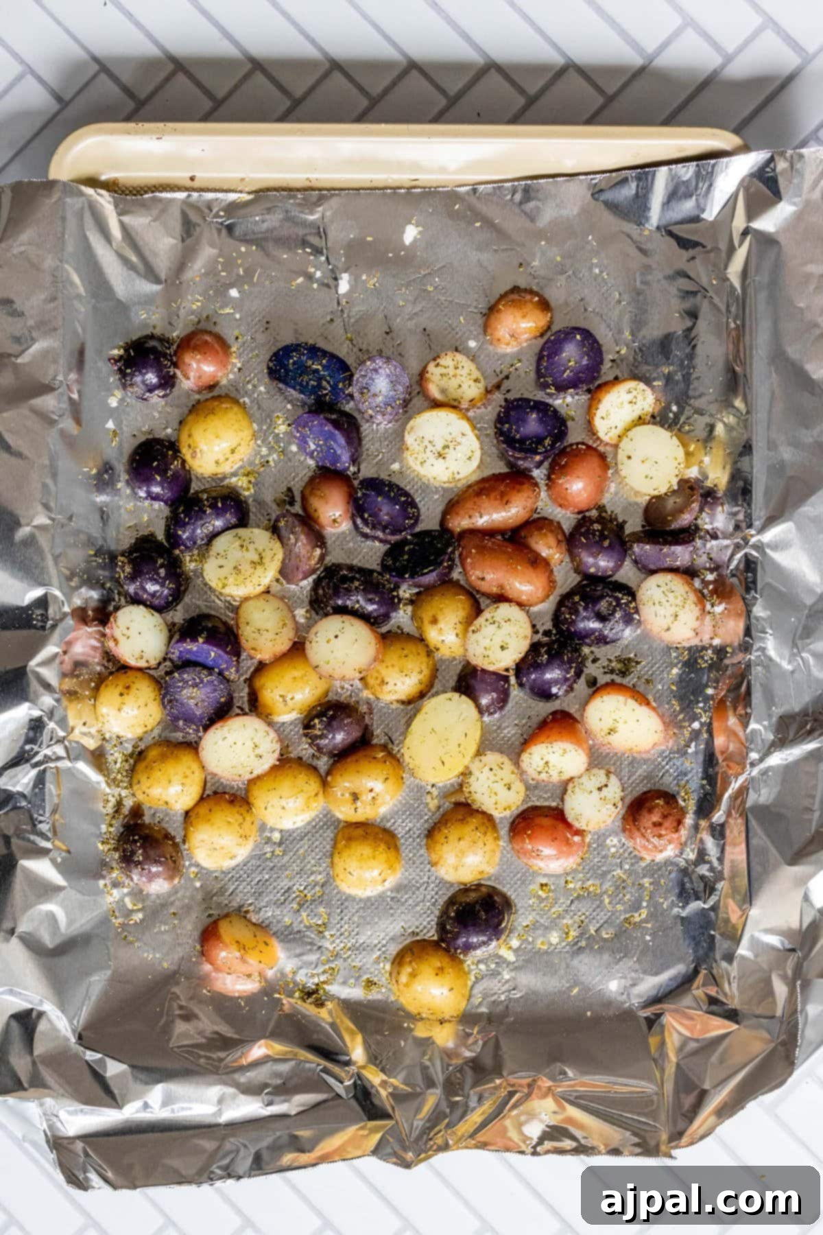 Potatoes spread on a baking sheet lined with foil, showing their seasoned state before grilling.