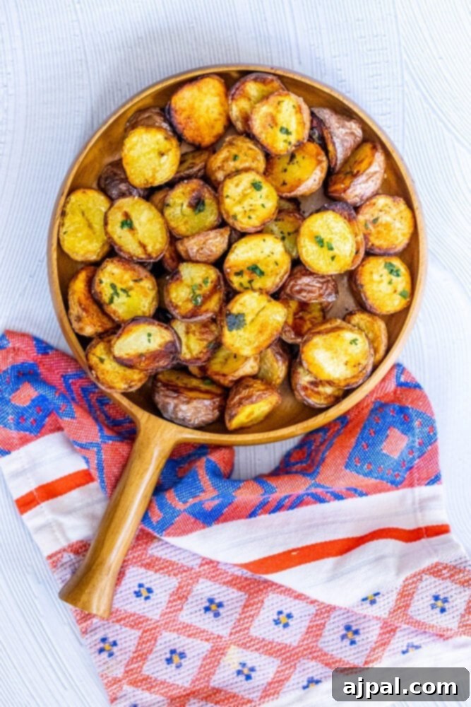 A wooden platter filled with golden, crispy grilled potatoes, generously garnished with fresh herbs and a sprinkle of salt.
