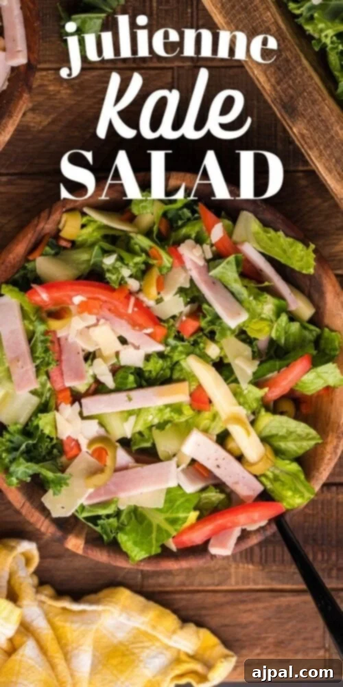 An appetizing picture of Julienne Kale Salad with meat, cheese, and vegetables, adorned with Mediterranean dressing, served in a rustic wood bowl on a wooden table.