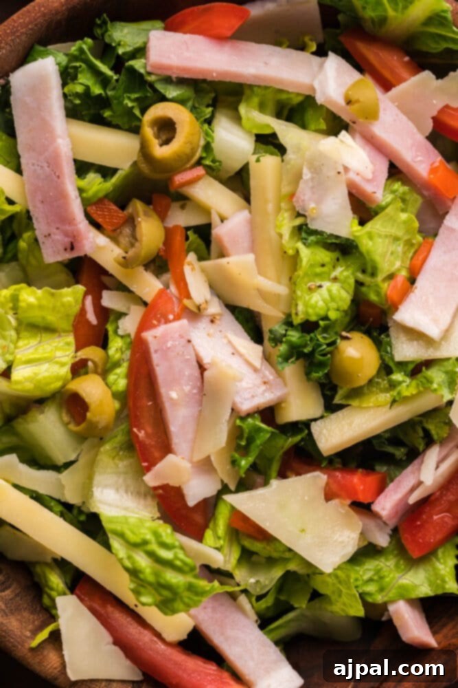 A close-up of Julienne Kale Salad with ham, tomatoes, and olives in a rustic wooden bowl, showcasing the fresh ingredients.