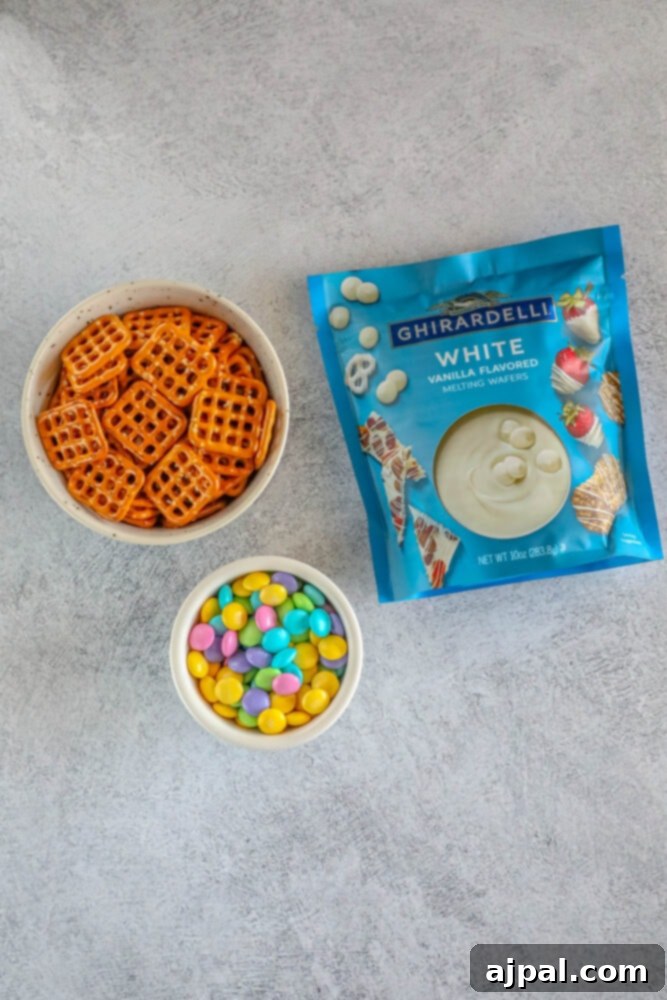 Hoppy Easter Pretzels 4 Ingredients for Easter Pretzel Snacks: chocolate wafers, M&Ms, and pretzels on a table.