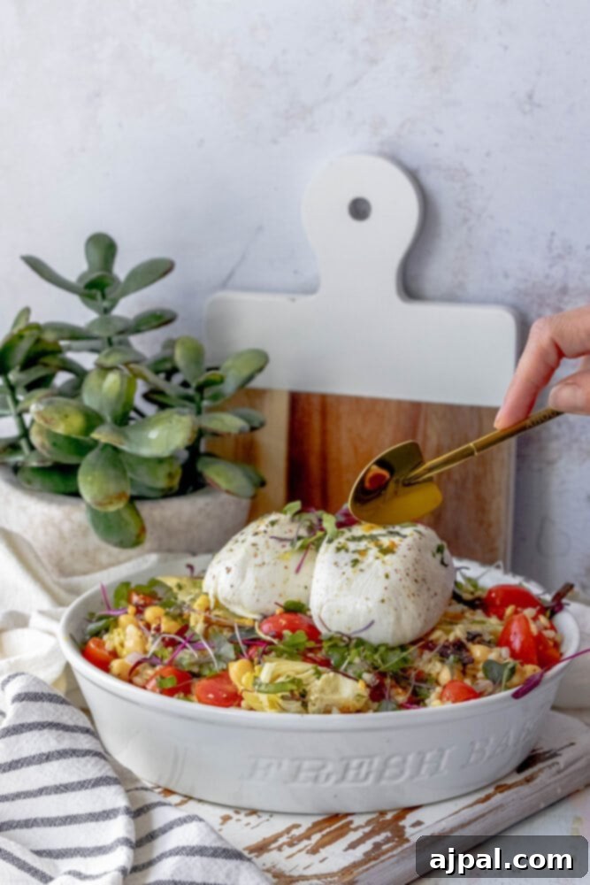 Close-up of a delectable Burrata Barley Salad in a white bowl, showcasing a rich medley of microgreens, succulent artichoke hearts, and vibrant cherry tomatoes.