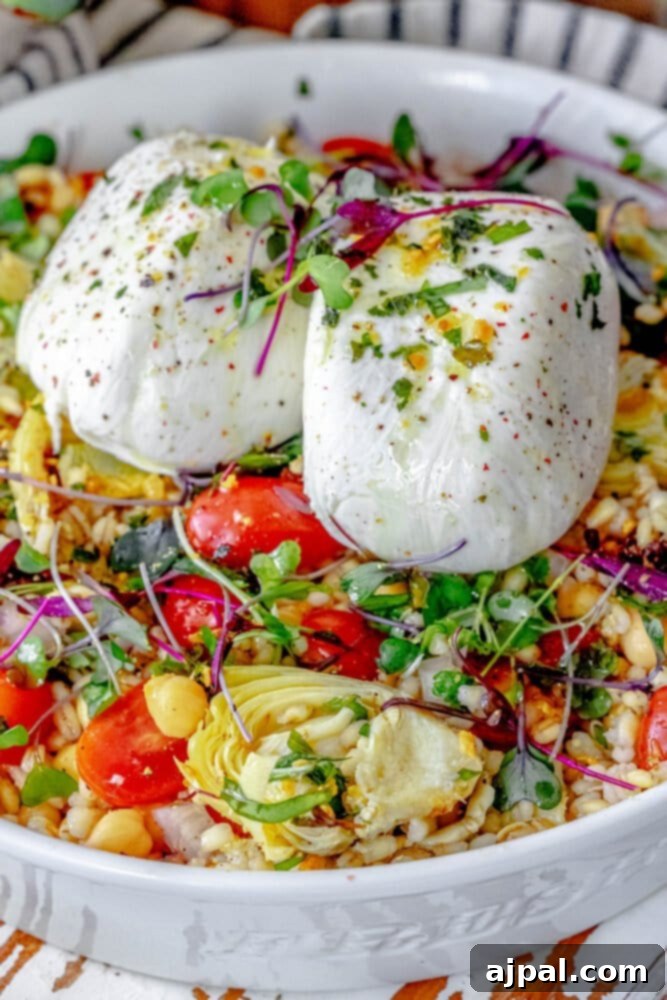 A vibrant Burrata Barley Salad presented in a white bowl, showcasing a medley of fresh microgreens, succulent artichoke hearts, and juicy tomatoes, inviting you to savor its flavors.