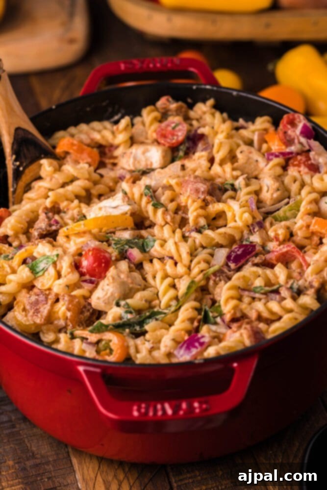 Velvet Chicken Bacon Pasta Salad 12 A large serving of creamy chicken bacon pasta salad, presented in a red skillet with a mix of colorful vegetables.