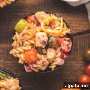 A vibrant bowl of creamy chicken bacon pasta salad, brimming with tender chicken, crispy bacon, and colorful vegetables, all coated in a rich dressing.