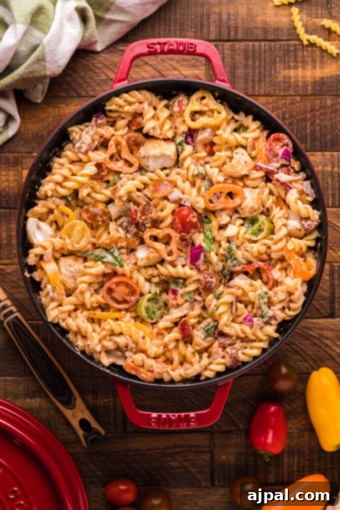 Velvet Chicken Bacon Pasta Salad 10 A large bowl of creamy chicken bacon pasta salad, filled with colorful vegetables, ready to be served on a wooden table.