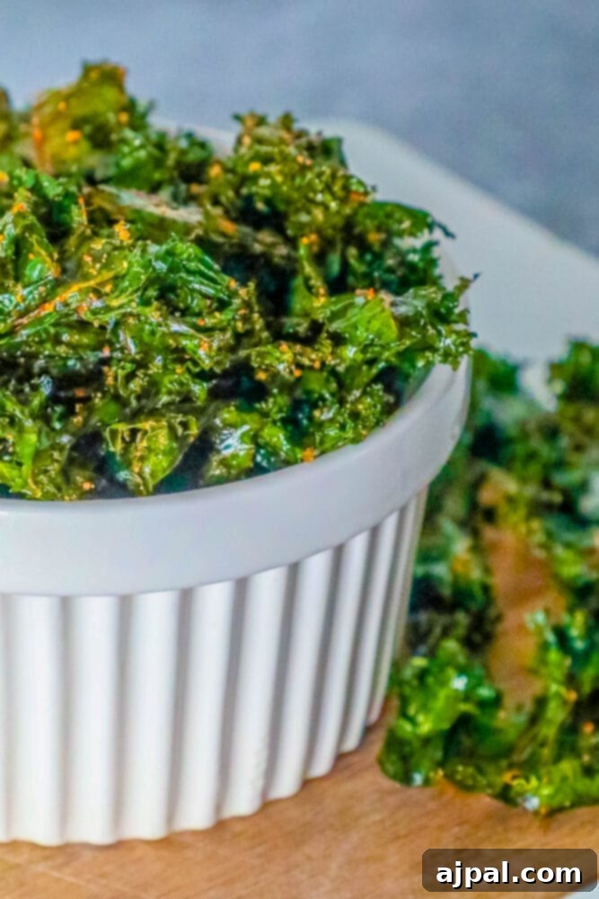 A crisp bowl of golden-green kale chips, perfectly baked and ready to enjoy, resting on a clean white surface.