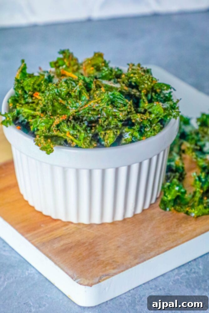 A pristine white bowl filled with golden-green kale chips, perfectly baked and ready for immediate enjoyment, rests on a simple cutting board.