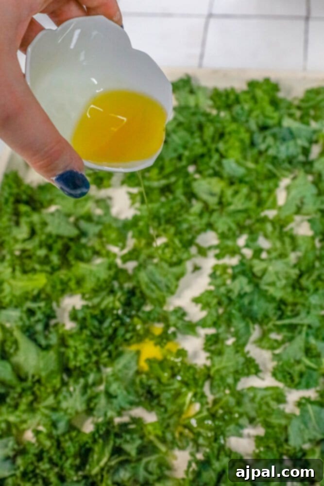 Olive oil is being carefully drizzled over torn kale leaves, preparing them for a gentle massage to ensure even coating.