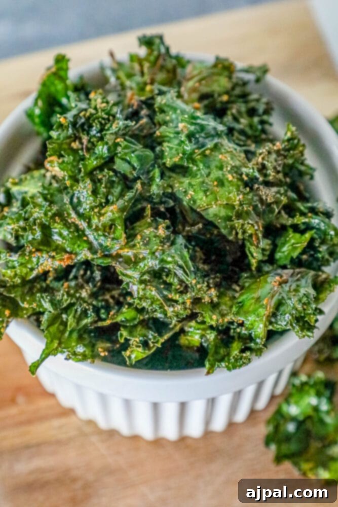 A bowl of freshly baked, golden-green kale chips rests on a rustic wooden cutting board, perfectly ready for snacking.