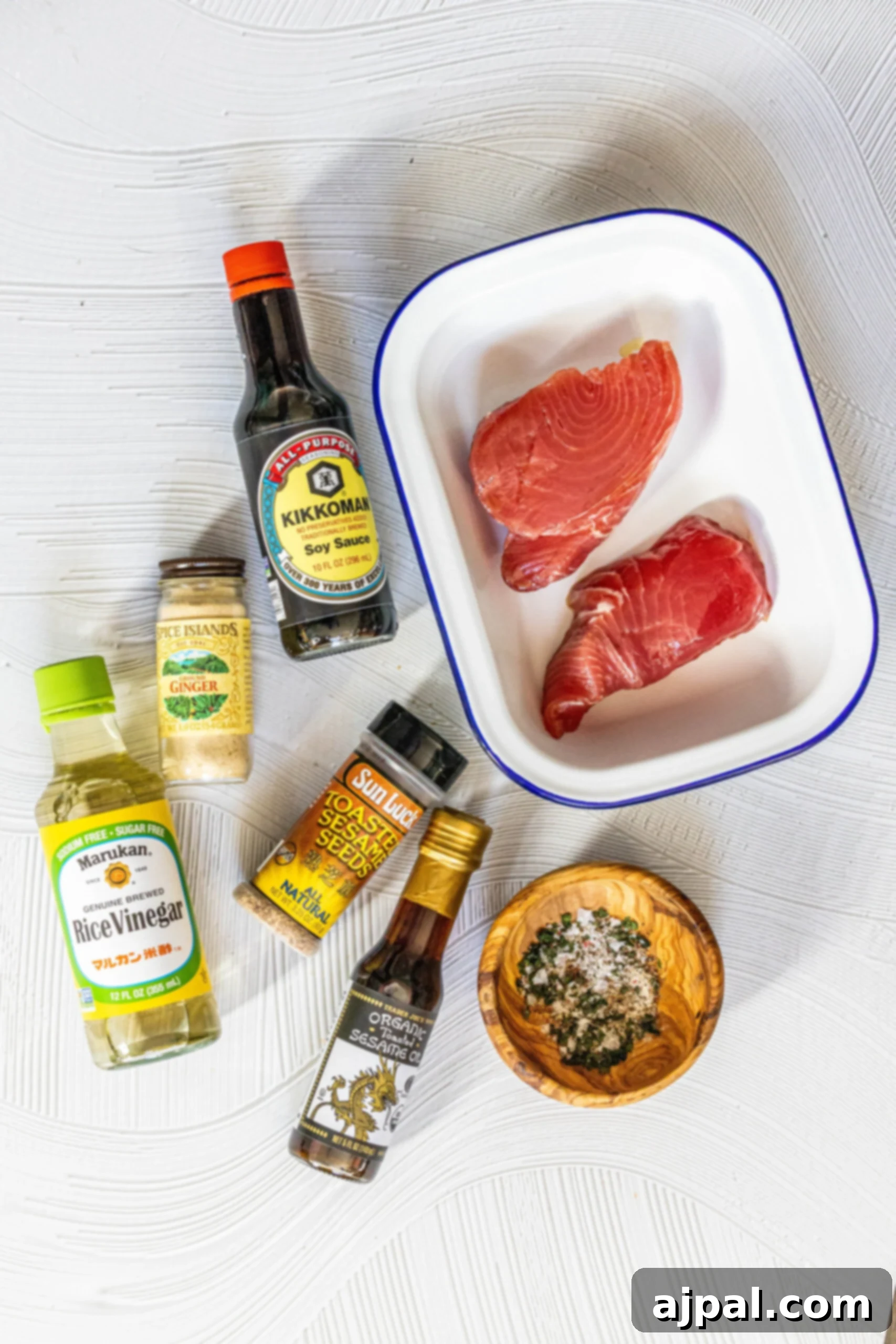 Seared Sesame Ahi with Tangy Ginger Soy 3 Ingredients for sesame ginger tuna steaks laid out on a table, including tuna steaks, soy sauce, ginger, sesame seeds, sesame oil, rice vinegar, and fresh herbs.