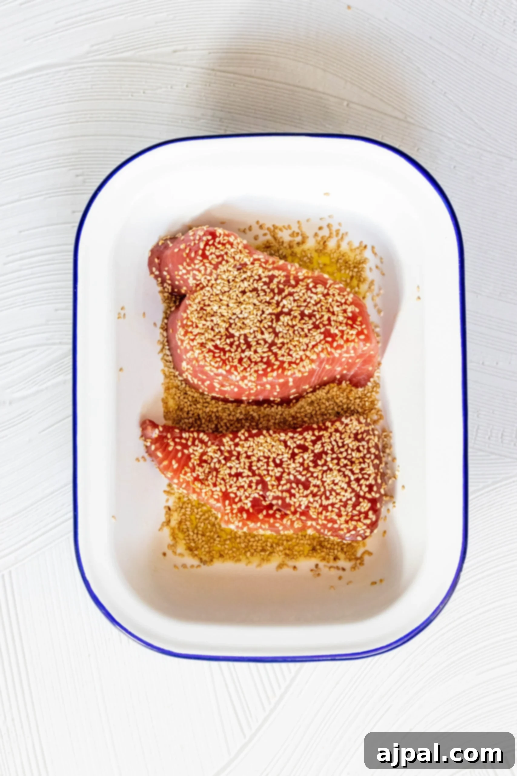 Seared Sesame Ahi with Tangy Ginger Soy 4 Close-up picture of tuna steaks generously coated with sesame seeds, marinating in a bowl.