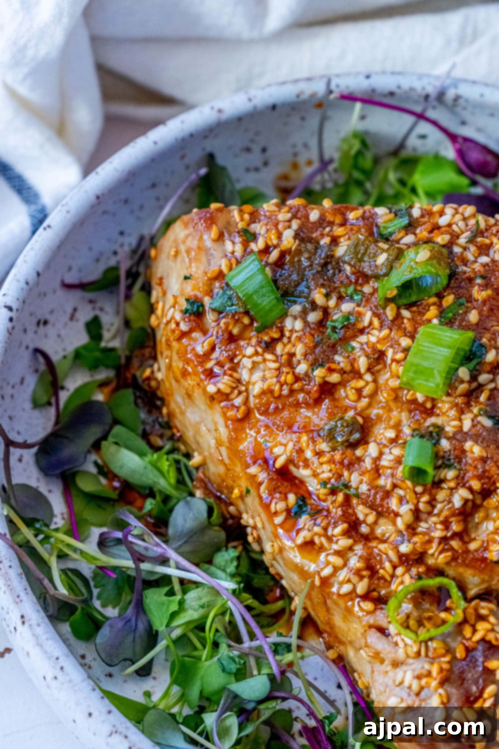 Seared Sesame Ahi with Tangy Ginger Soy 5 A vibrant bowl of grilled salmon (image description states salmon, but context implies tuna) with a sprinkle of sesame seeds and fresh green onions.