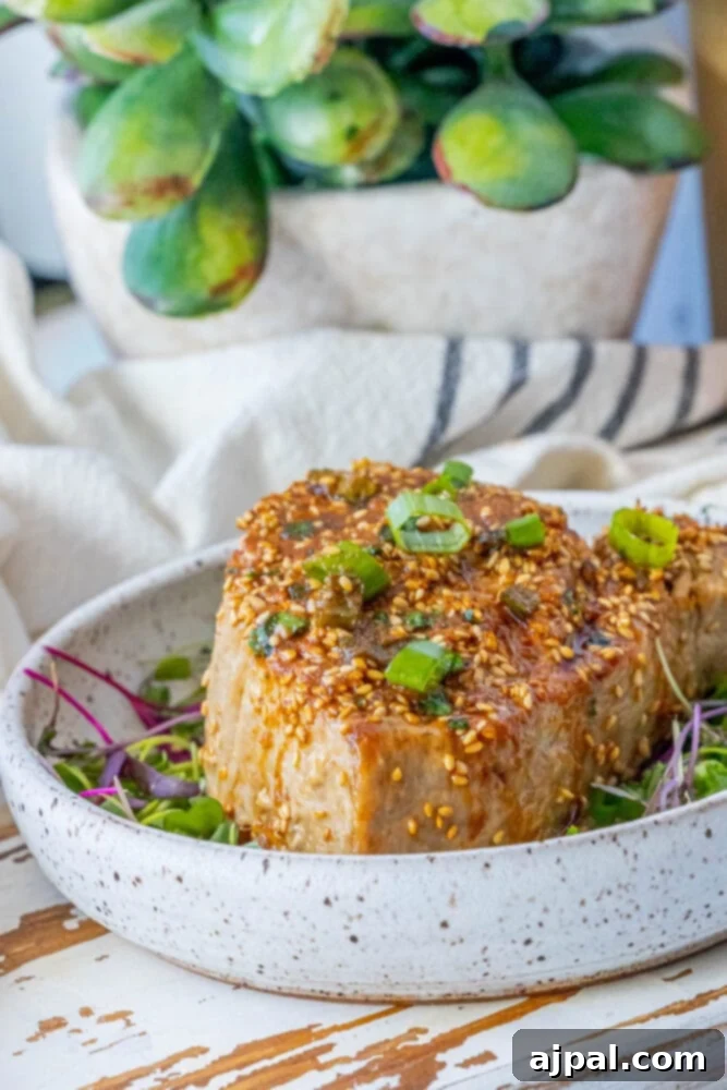 Seared Sesame Ahi with Tangy Ginger Soy 6 Another picture of a grilled tuna steak on a white plate, garnished with sesame seeds and green onions.