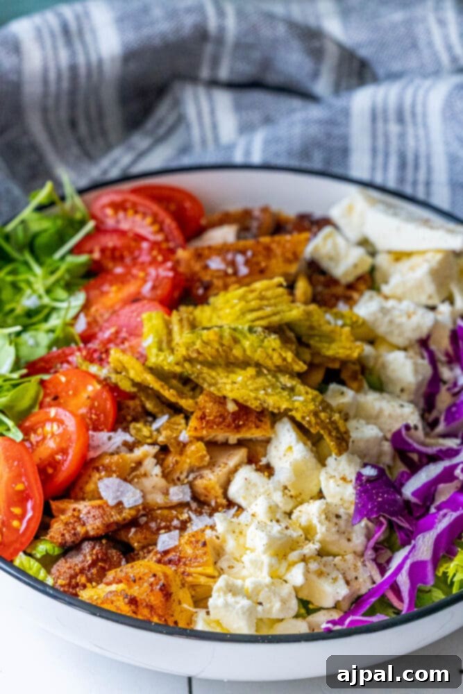 Spicy Jalapeno Chicken Thigh Salad 2 A vibrant bowl filled with lettuce, bean sprouts, cherry tomatoes, purple cabbage, crispy grilled chicken, crumbled feta, and spicy jalapeno chips. It's a fresh and colorful meal perfect for lunch.