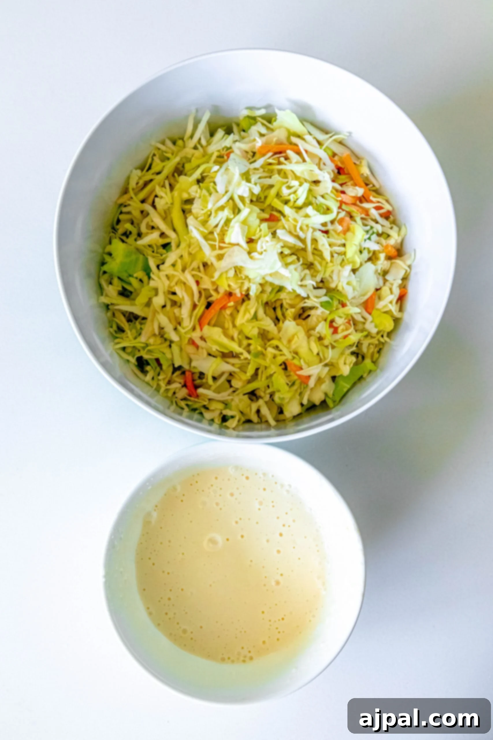 Quick & Easy 4-Ingredient Coleslaw 5 Homemade coleslaw dressing in a small bowl, with shredded cabbage and carrots ready to be mixed.