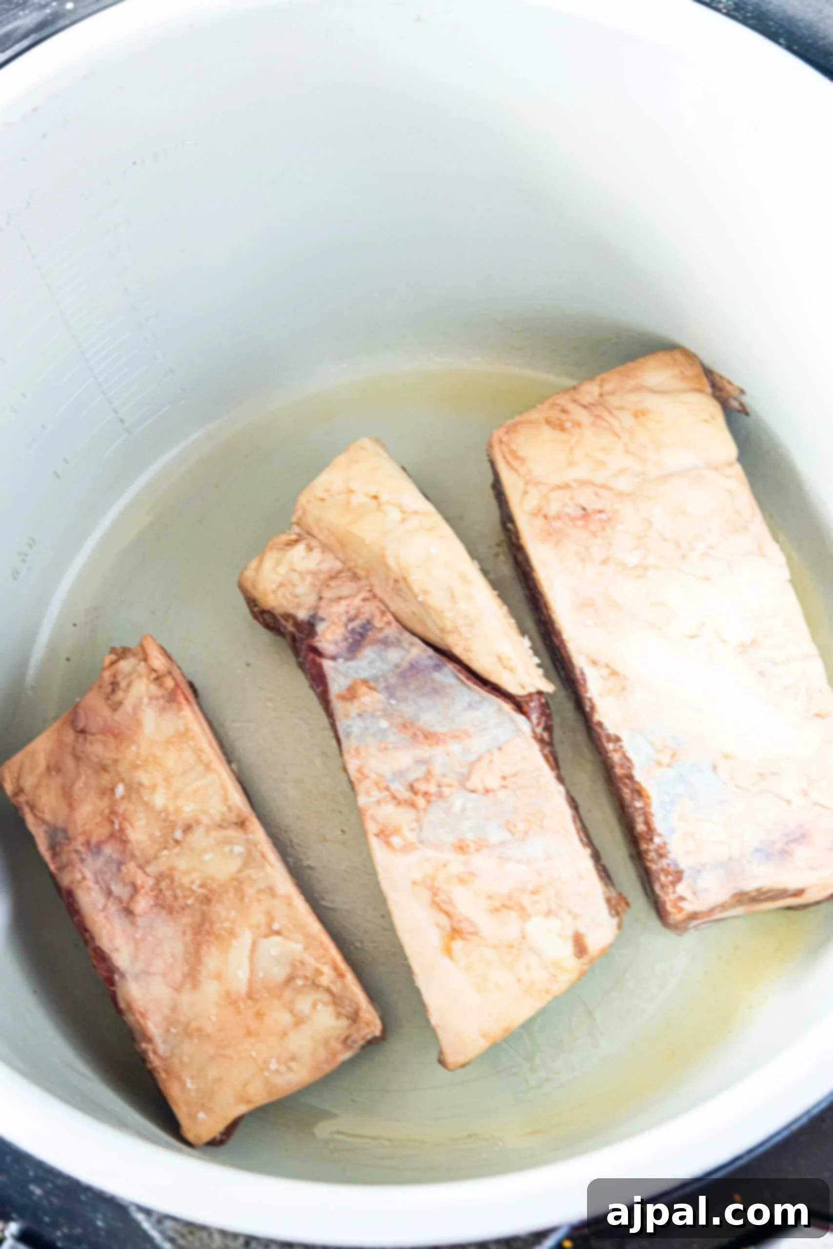 Three pieces of beef short ribs are being cooked in an Instant Pot.