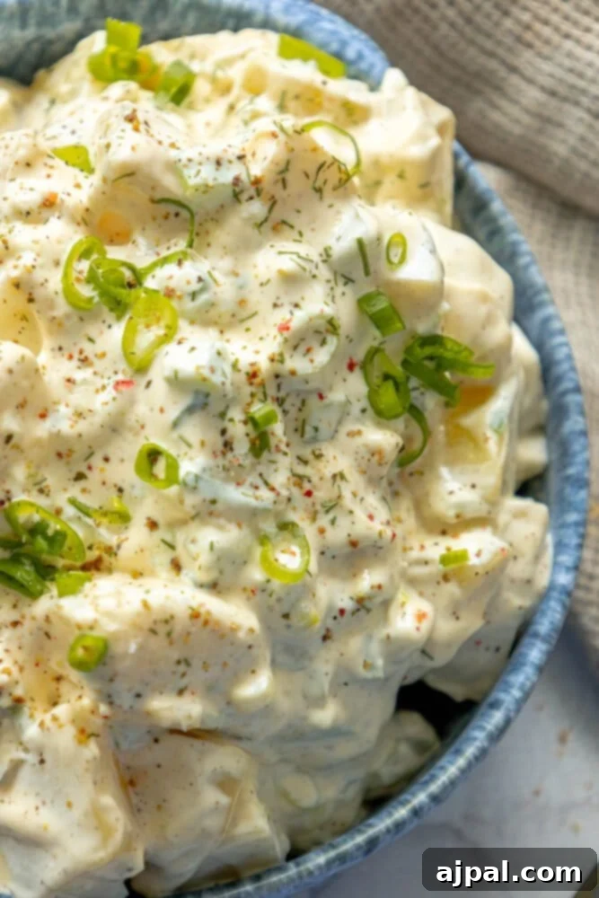 Simple & Scrumptious Potato Salad 2 Picture of creamy potato salad with green onions and cracked pepper in a blue bowl.
