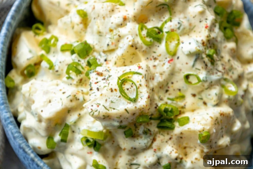 Simple & Scrumptious Potato Salad 11 Picture of creamy potato salad with green onions and cracked pepper in a blue bowl, garnished with fresh chives and dill.