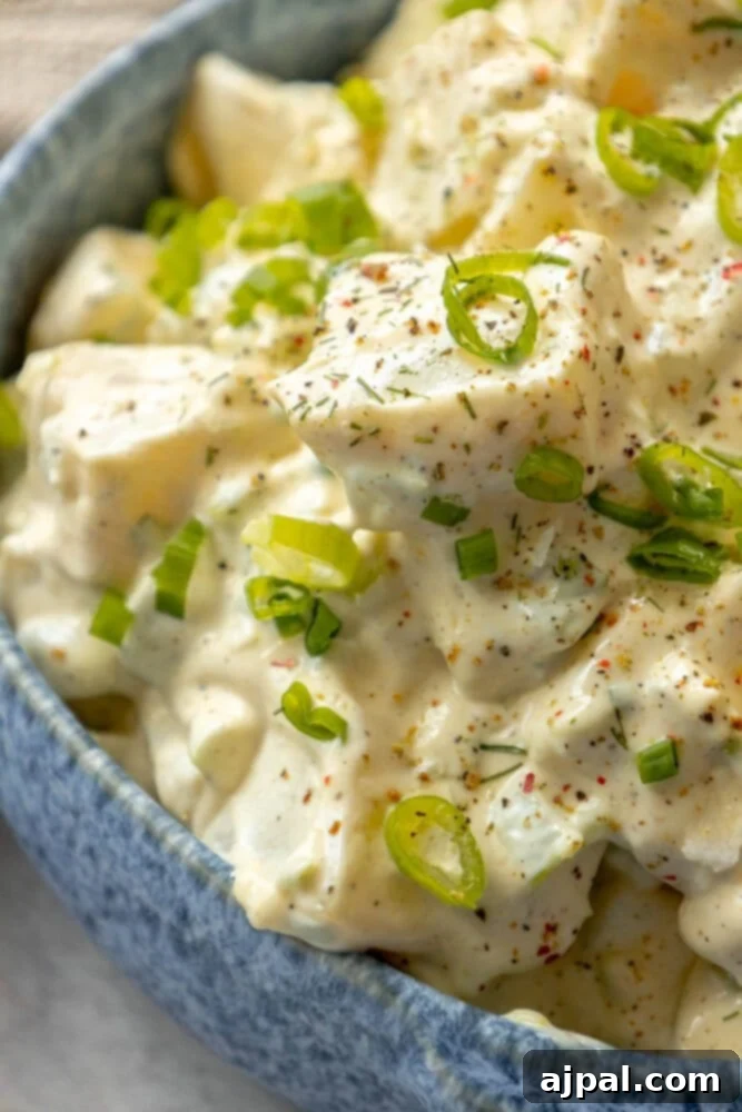 Simple & Scrumptious Potato Salad 12 Picture of creamy potato salad with green onions and cracked pepper in a blue bowl, garnished with fresh herbs.