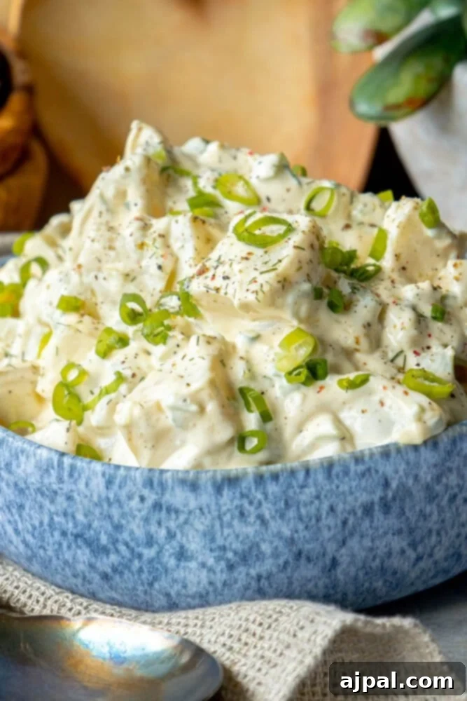 Simple & Scrumptious Potato Salad 3 Picture of creamy potato salad with green onions and cracked pepper in a blue bowl, garnished with fresh herbs.